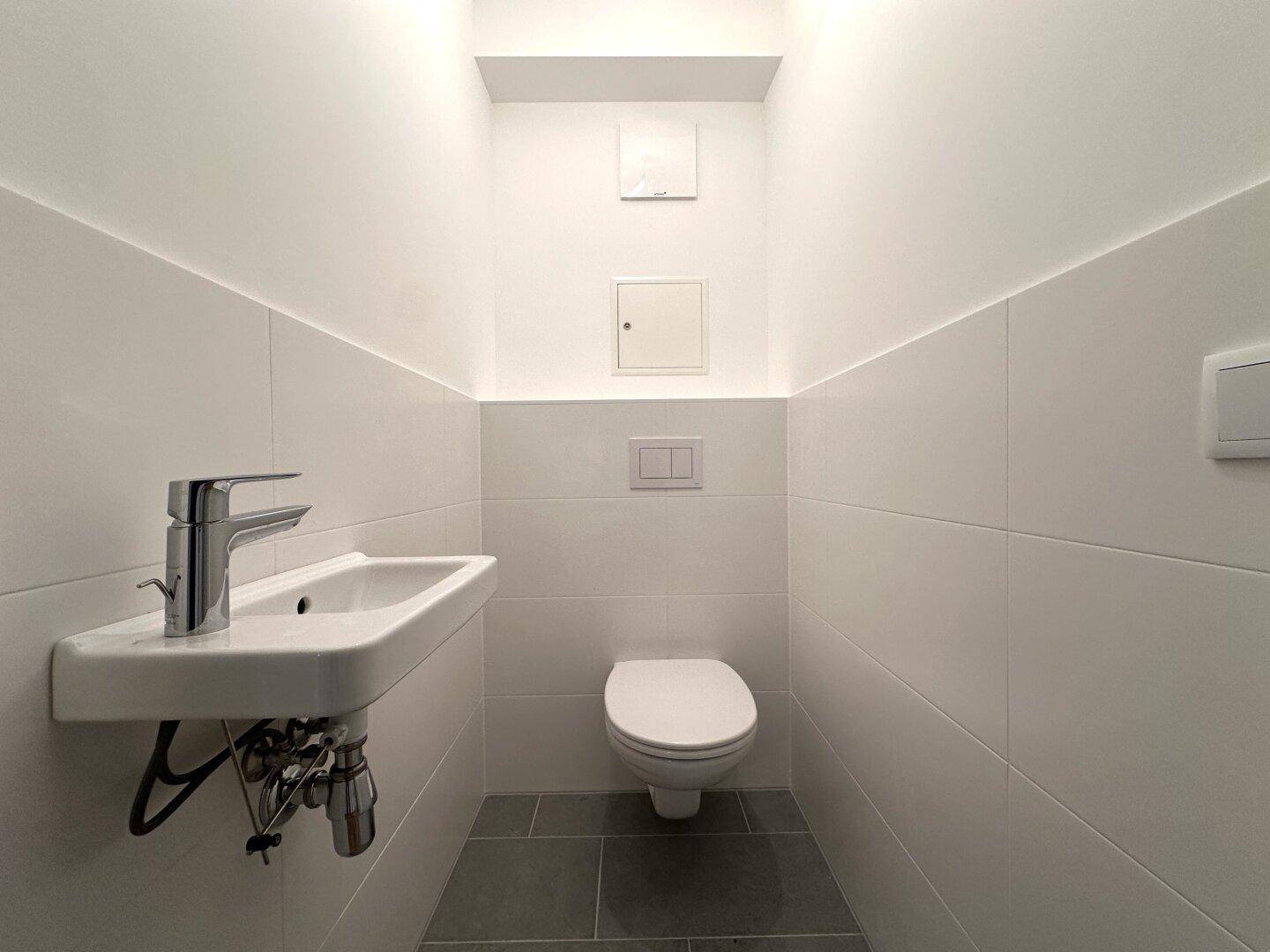 Modernes Gäste-WC mit wandhängender Toilette und kleinem Waschbecken, in schlichtem Design.