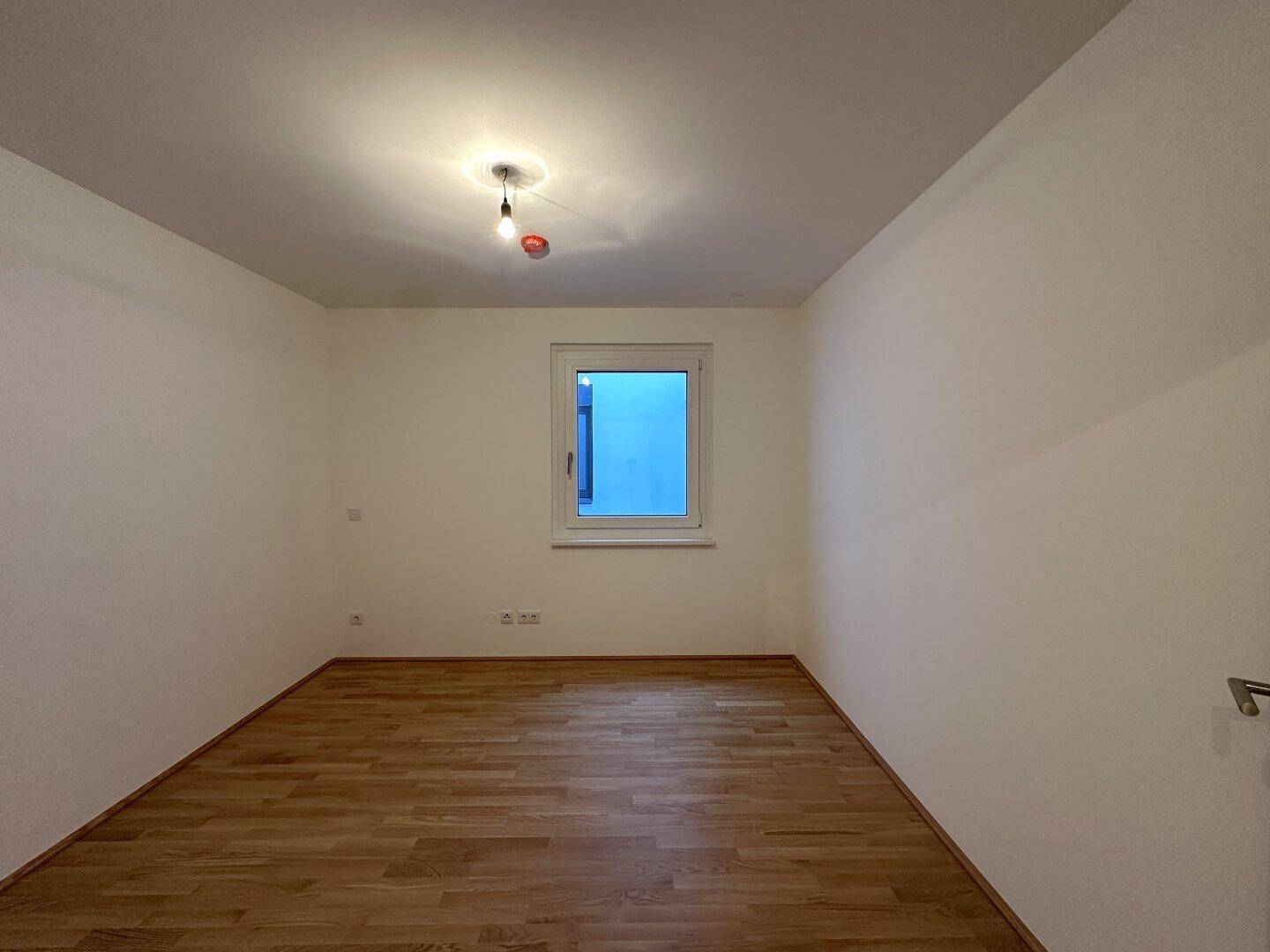 Weiteres helles Zimmer mit Parkettboden und einem Fenster.