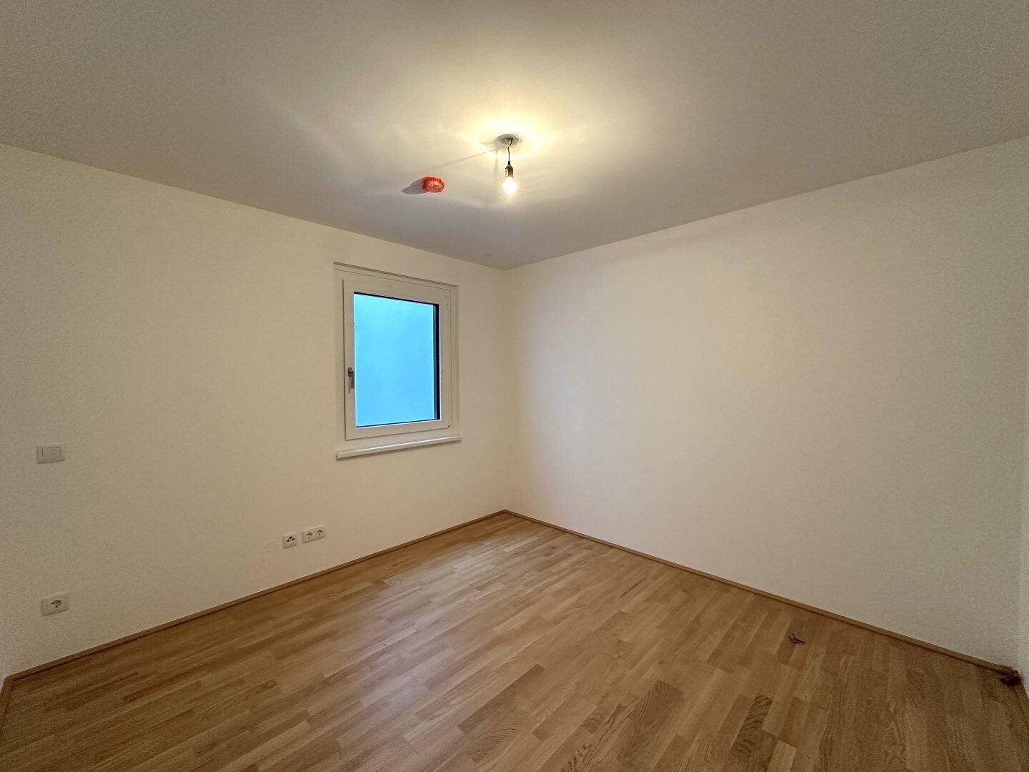 Leeres Zimmer mit Holzboden und weiß gestrichenen Wänden, bereit zum Einrichten.