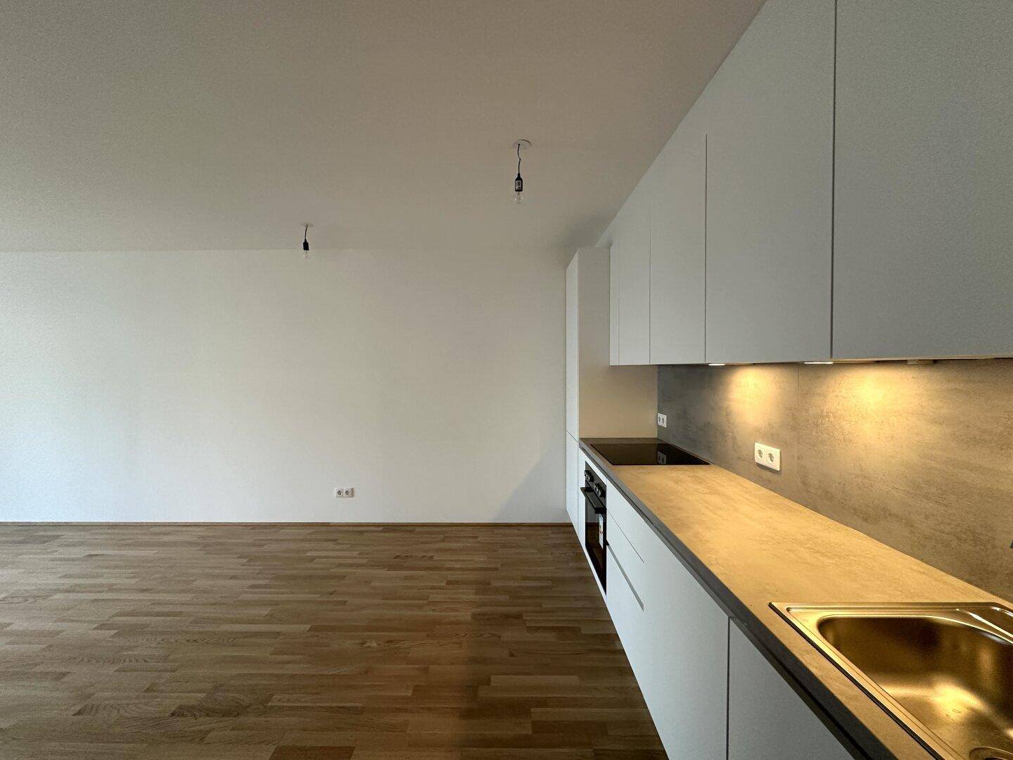 Moderne Küchenzeile mit weißen Schränken, Arbeitsplatte und integriertem Kochfeld.