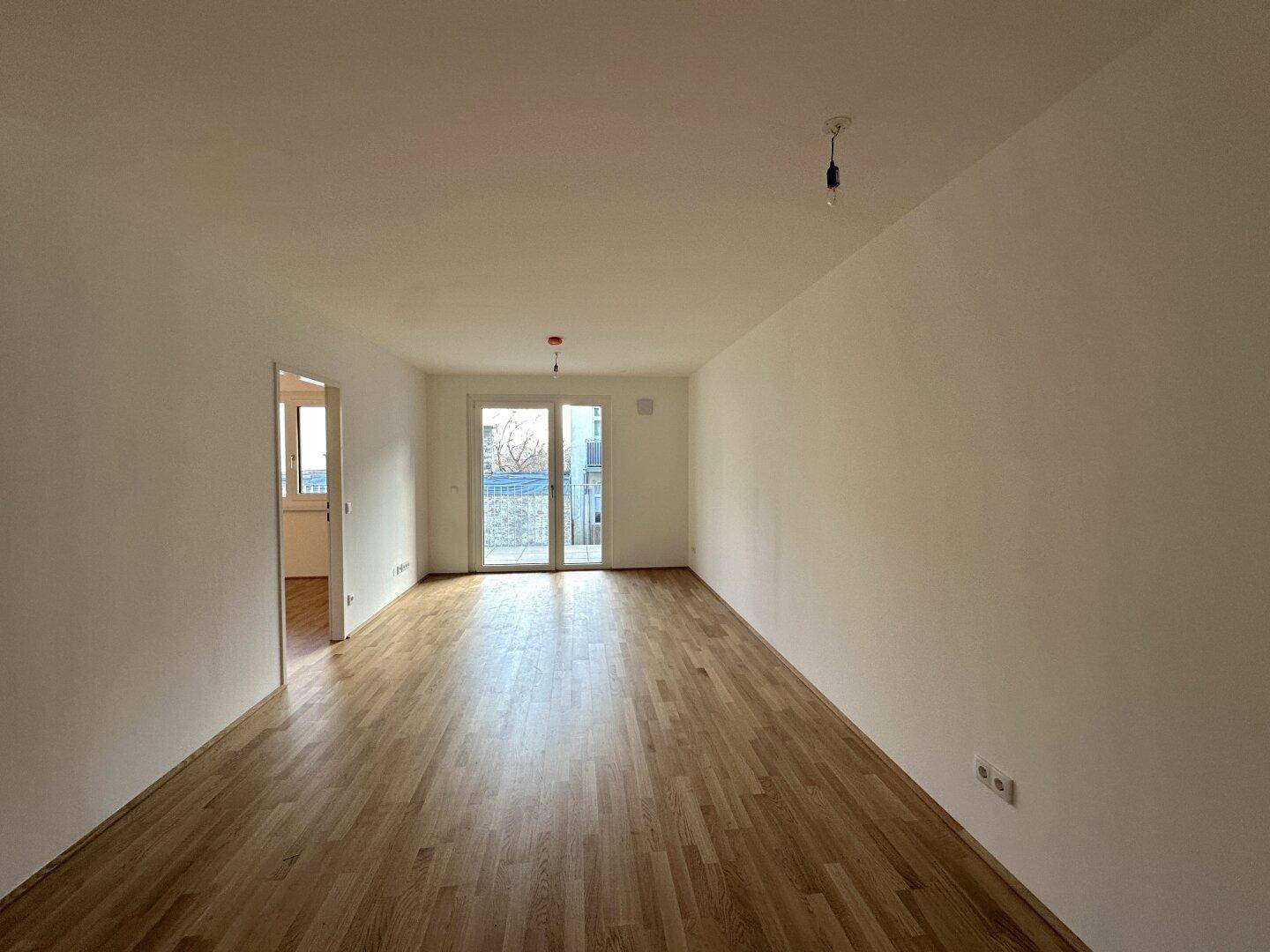 Geräumiger Wohnbereich mit Holzboden und Zugang zu einem Balkon.