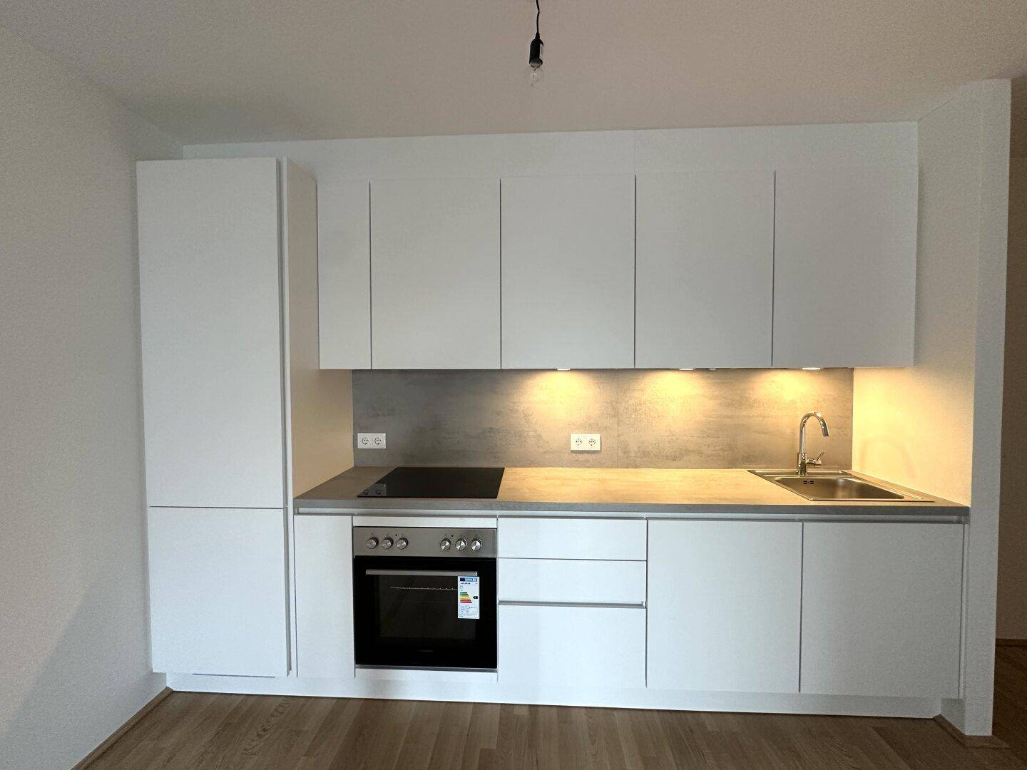 Neue, weiße Einbauküche mit Kochfeld, Backofen und viel Stauraum.