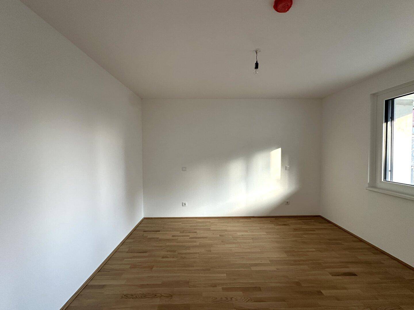 Helles Schlafzimmer mit Parkettboden und einem Fenster, das viel Licht hereinlässt.