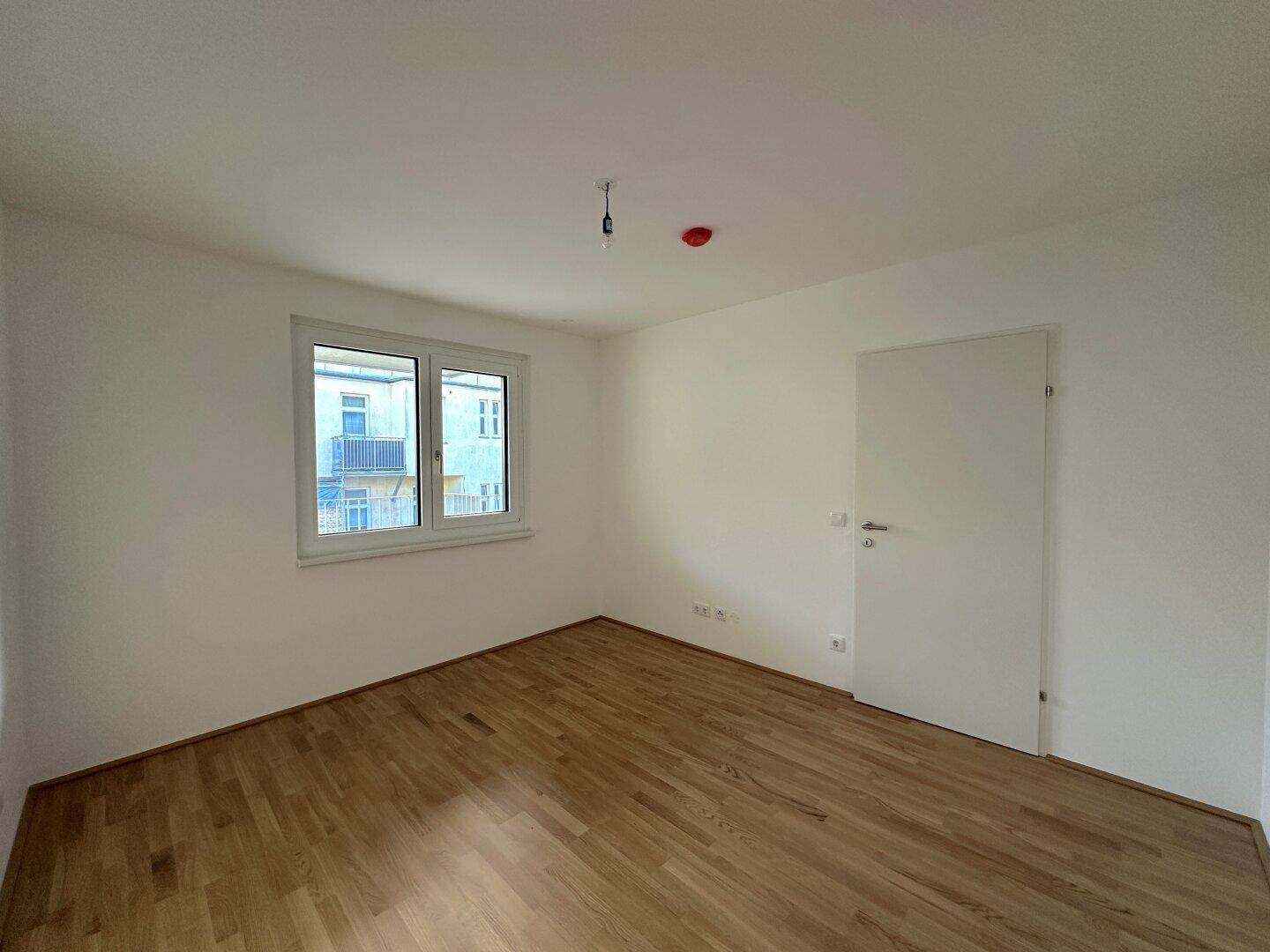 Leeres Schlafzimmer mit Holzboden und weiß gestrichenen Wänden.