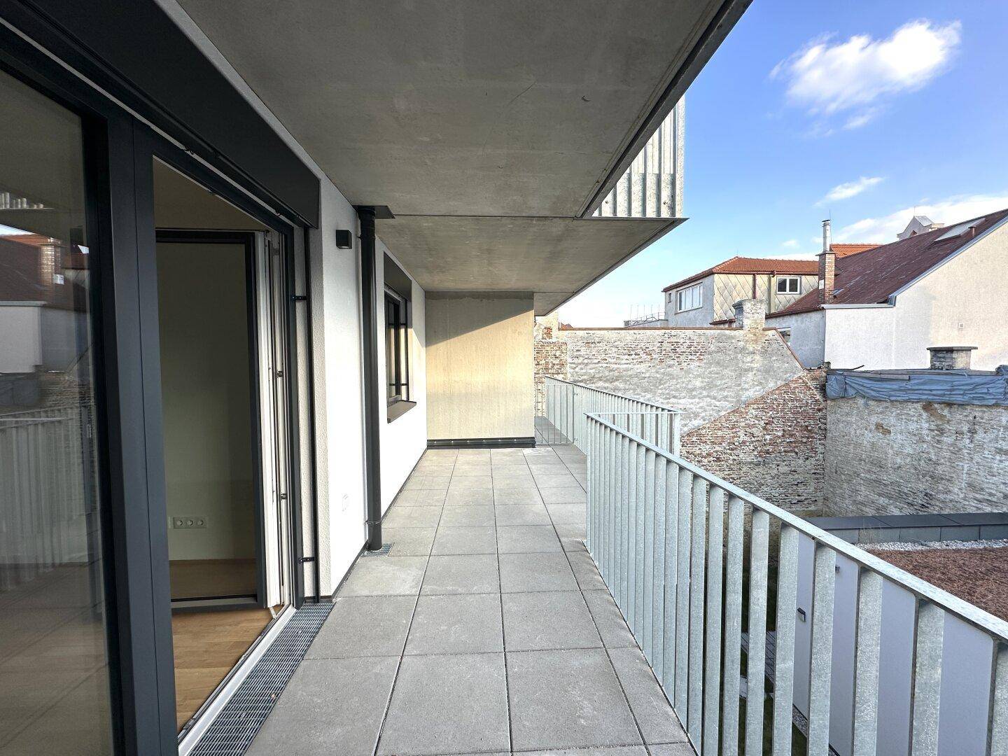 Langer, gefliester Balkon mit Metallgeländer und Blick auf die Umgebung.