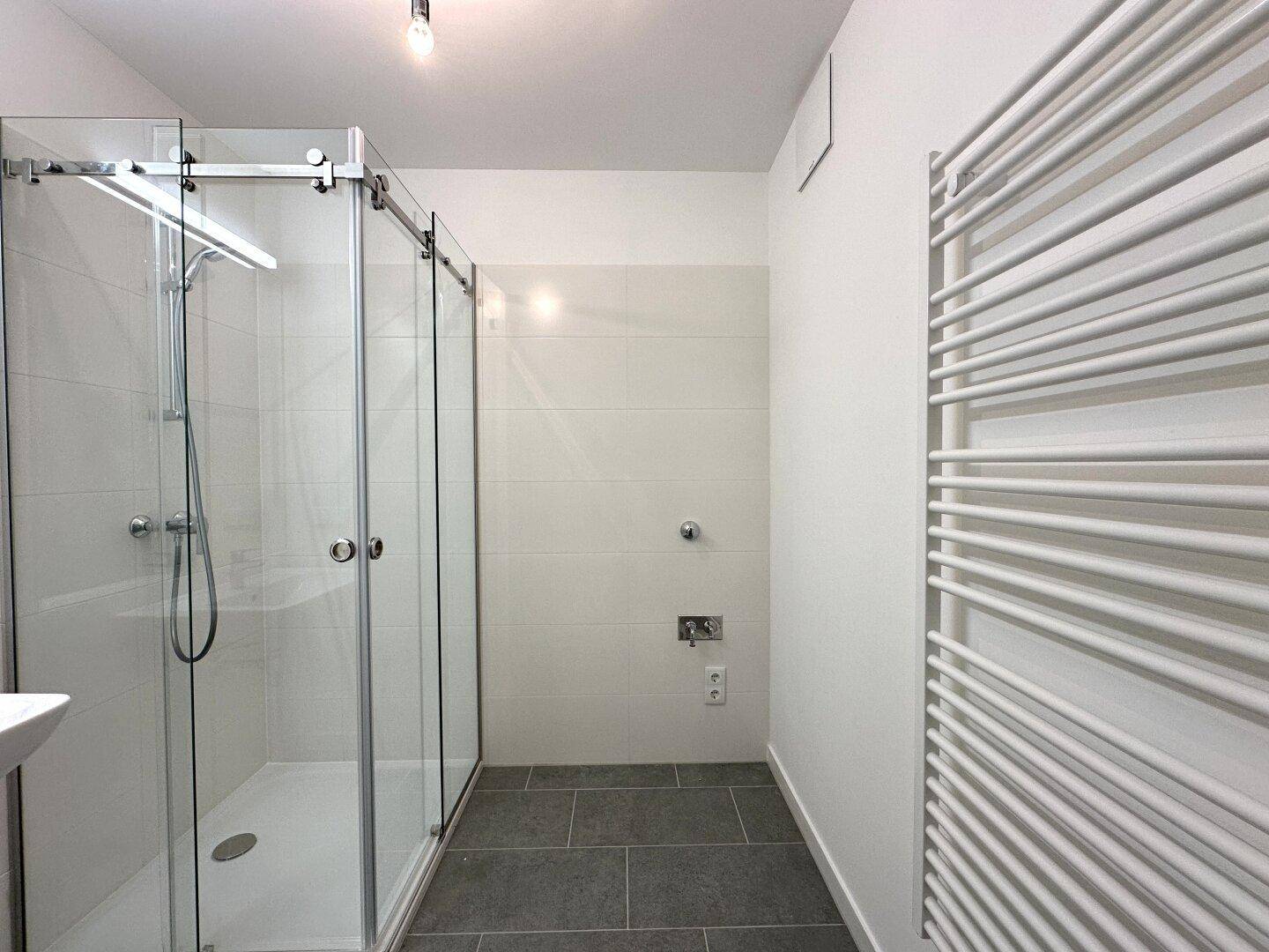 Helles Badezimmer mit großer Duschkabine und Fliesenboden.