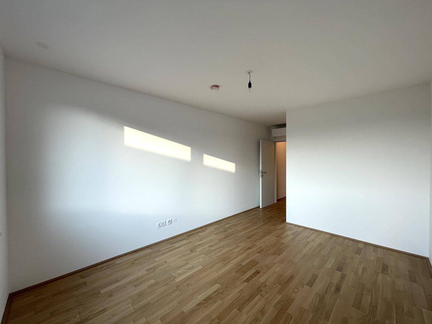 Lichtdurchflutetes Zimmer mit Holzboden und weißen Wänden, das viel natürliches Licht erhält.