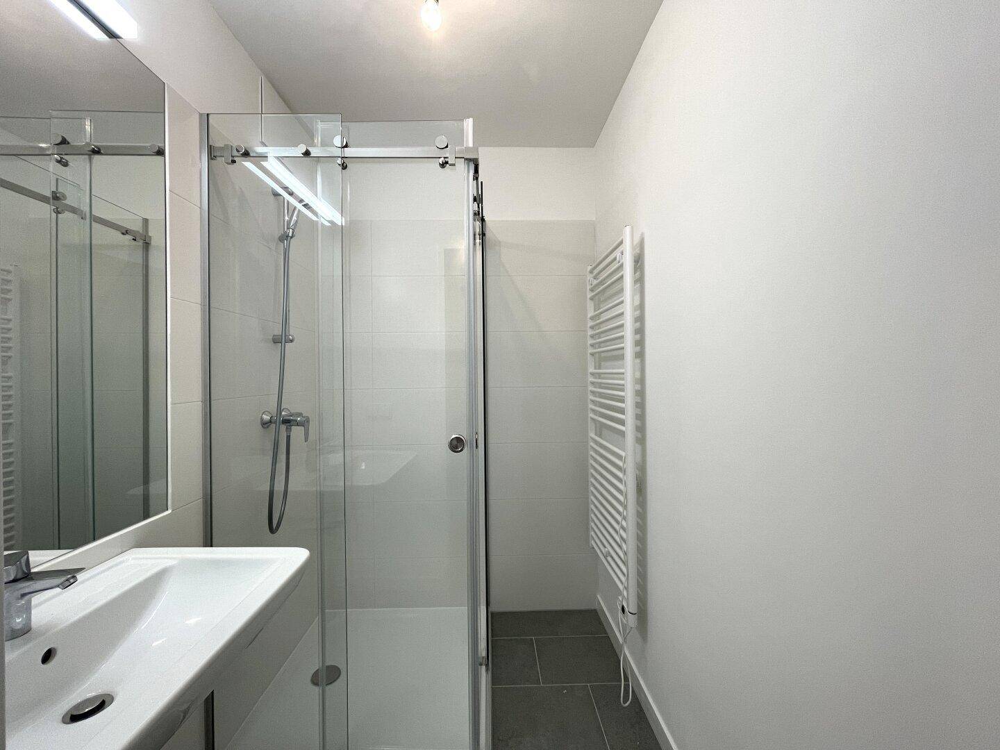 Modernes Badezimmer mit Duschkabine, Waschbecken, Spiegel und beheiztem Handtuchhalter.