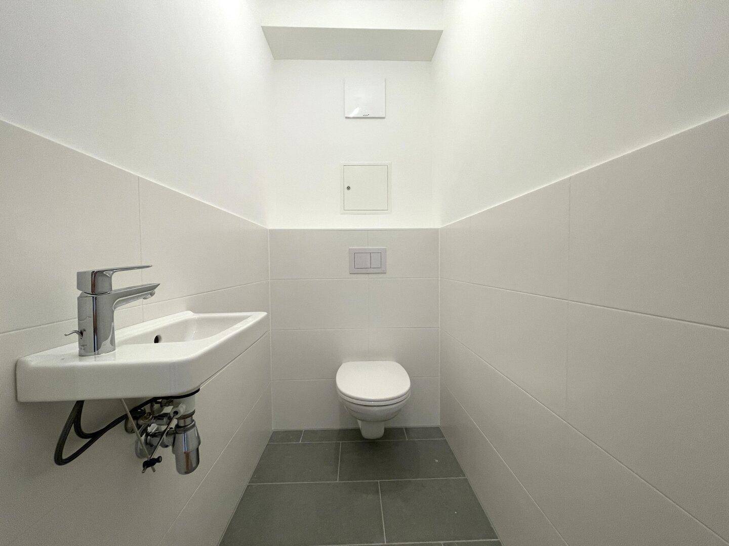 Modernes Gäste-WC mit wandhängender Toilette und kleinem Waschbecken, in hellen Fliesen gehalten.