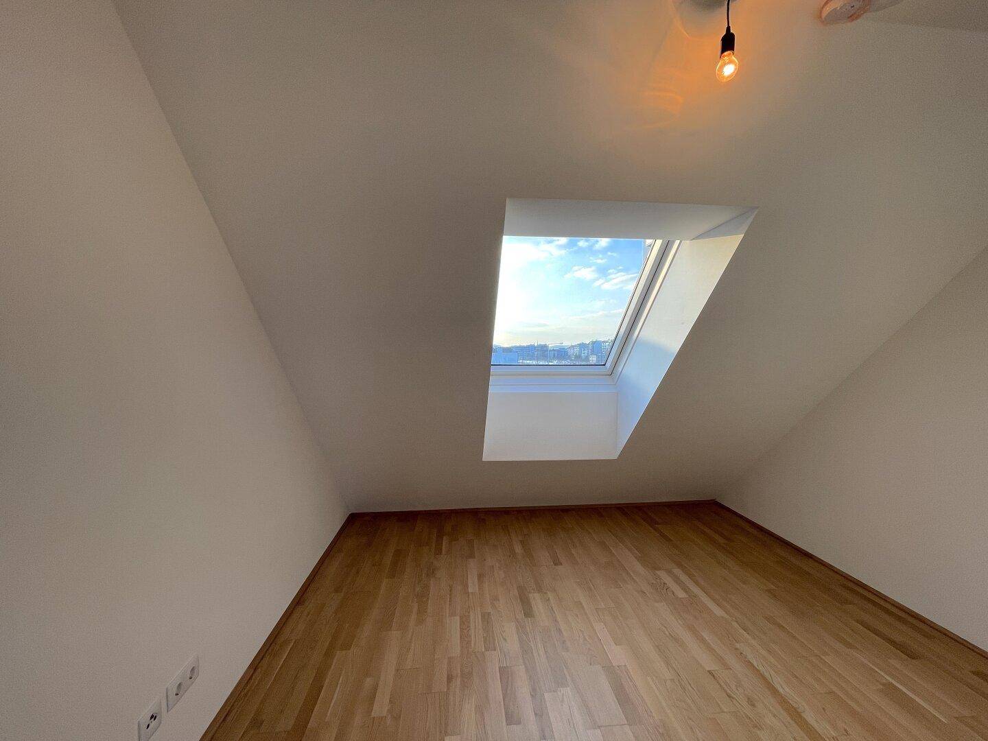 Gemütliches Zimmer im Dachgeschoss mit Holzboden, schräger Decke und einem hellen Dachfenster.
