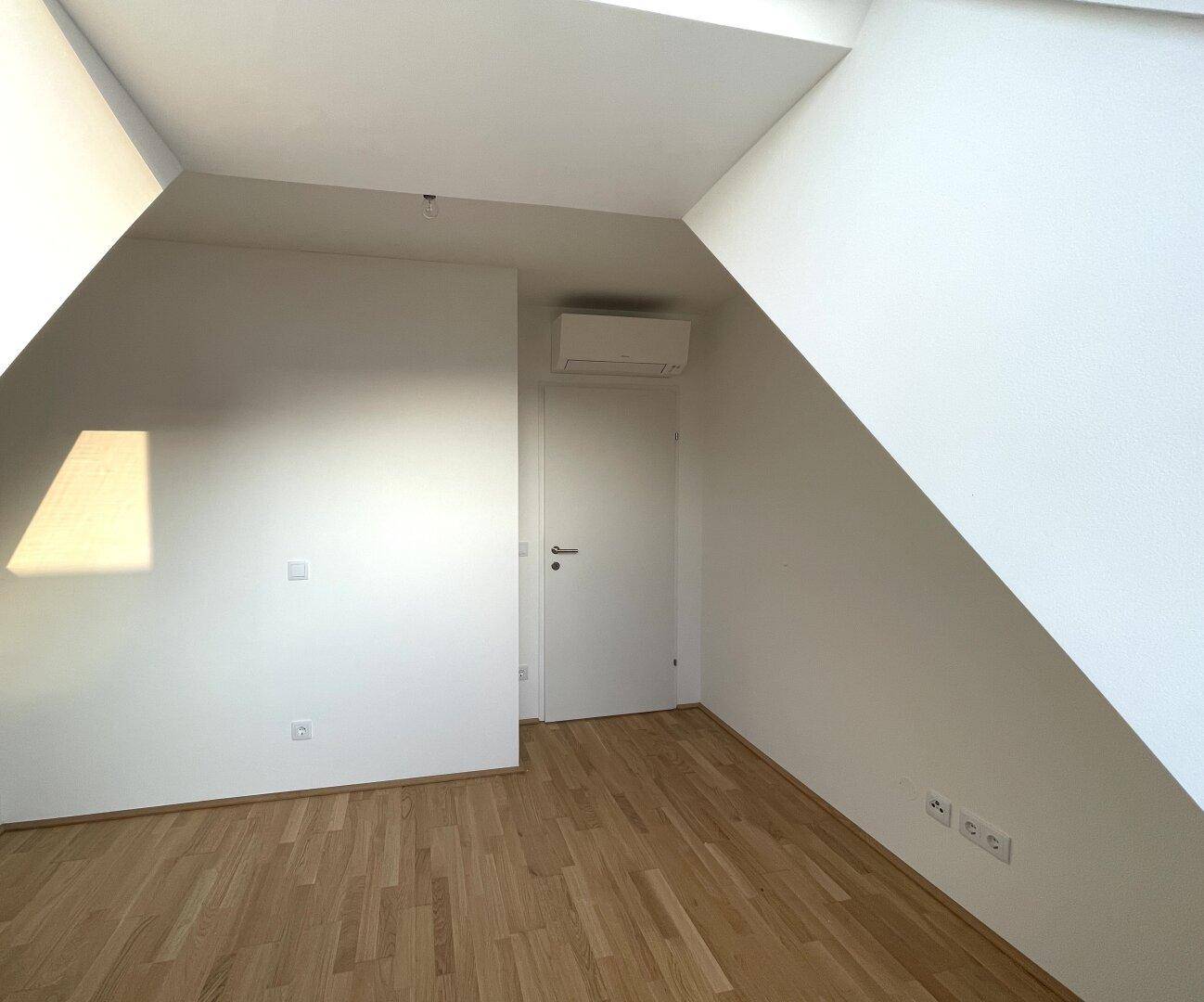 Dachzimmer mit Holzboden, schräger Decke und einer Klimaanlage für angenehme Temperaturen.