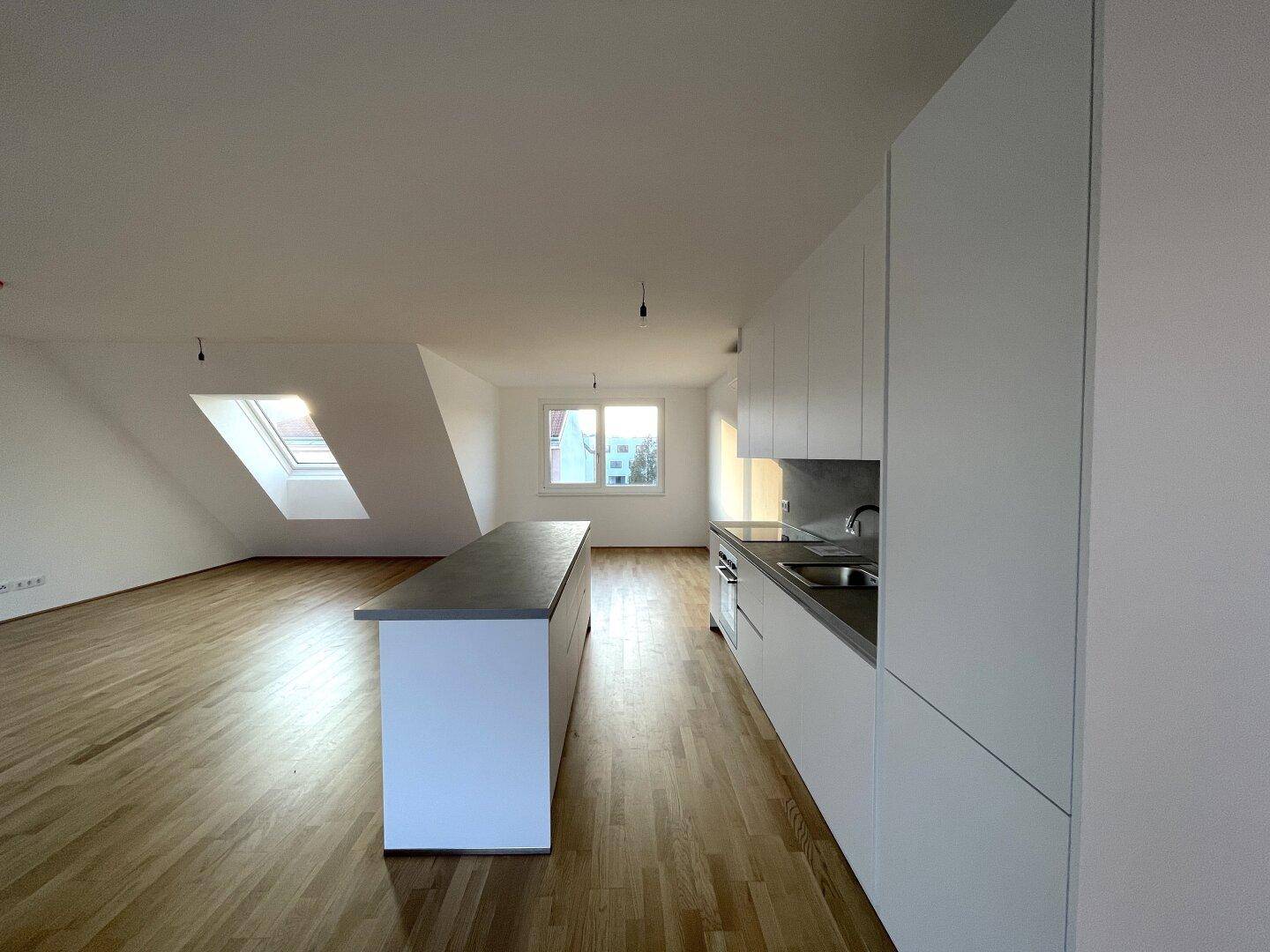 Moderne Einbauküche mit weißen Schränken, grauen Arbeitsplatten und einer Kücheninsel im offenen Wohnbereich.