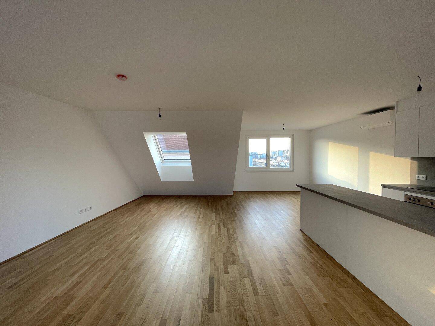 Geräumiger Wohnbereich mit hellem Holzboden und schrägen Wänden, durch Dachfenster lichtdurchflutet.