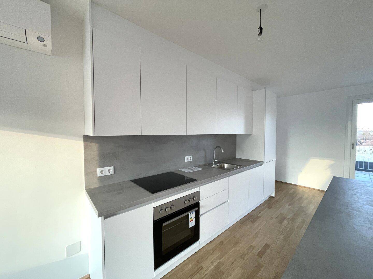 Helle, moderne Küche mit integriertem Backofen, Induktionskochfeld und Spülbecken, bereit zur Nutzung.