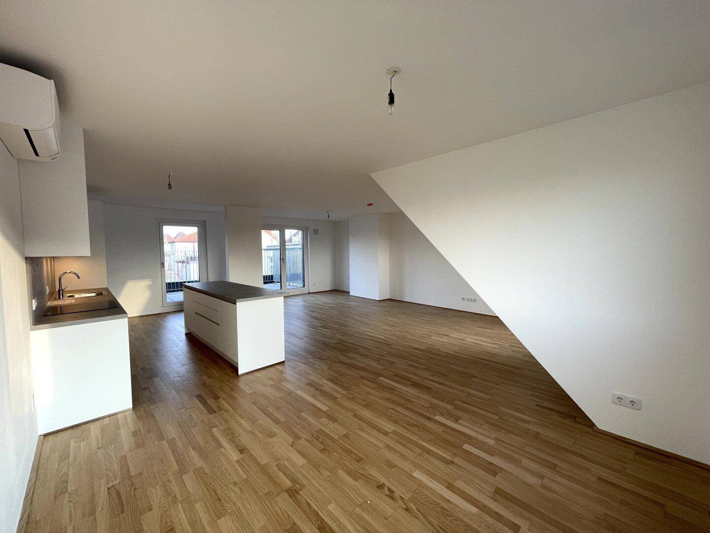 Offener Wohnbereich mit Kücheninsel und Zugang zu einer Außenterrasse durch große Glastüren.