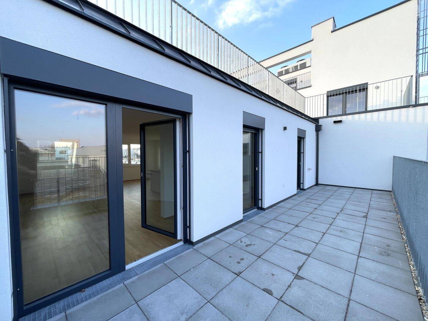Geräumige Dachterrasse mit grauen Fliesen und großen Glastüren, die in den Wohnbereich führen.