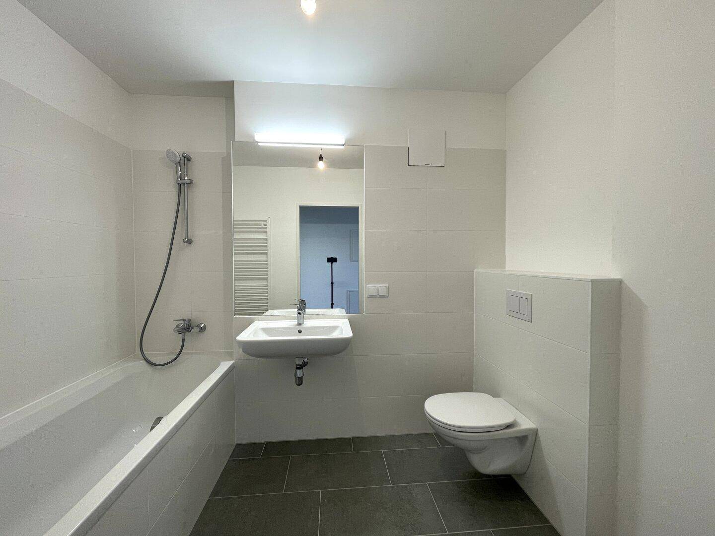 Modernes Badezimmer mit Badewanne, Waschbecken, Toilette und beheiztem Handtuchhalter, hell gefliest.