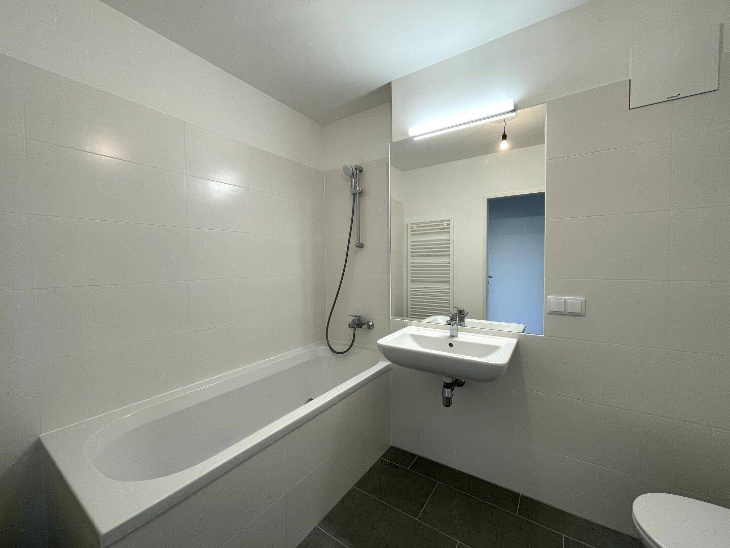 Helles Badezimmer mit Badewanne, modernem Waschbecken und Toilette, ausgestattet mit weißen Fliesen.
