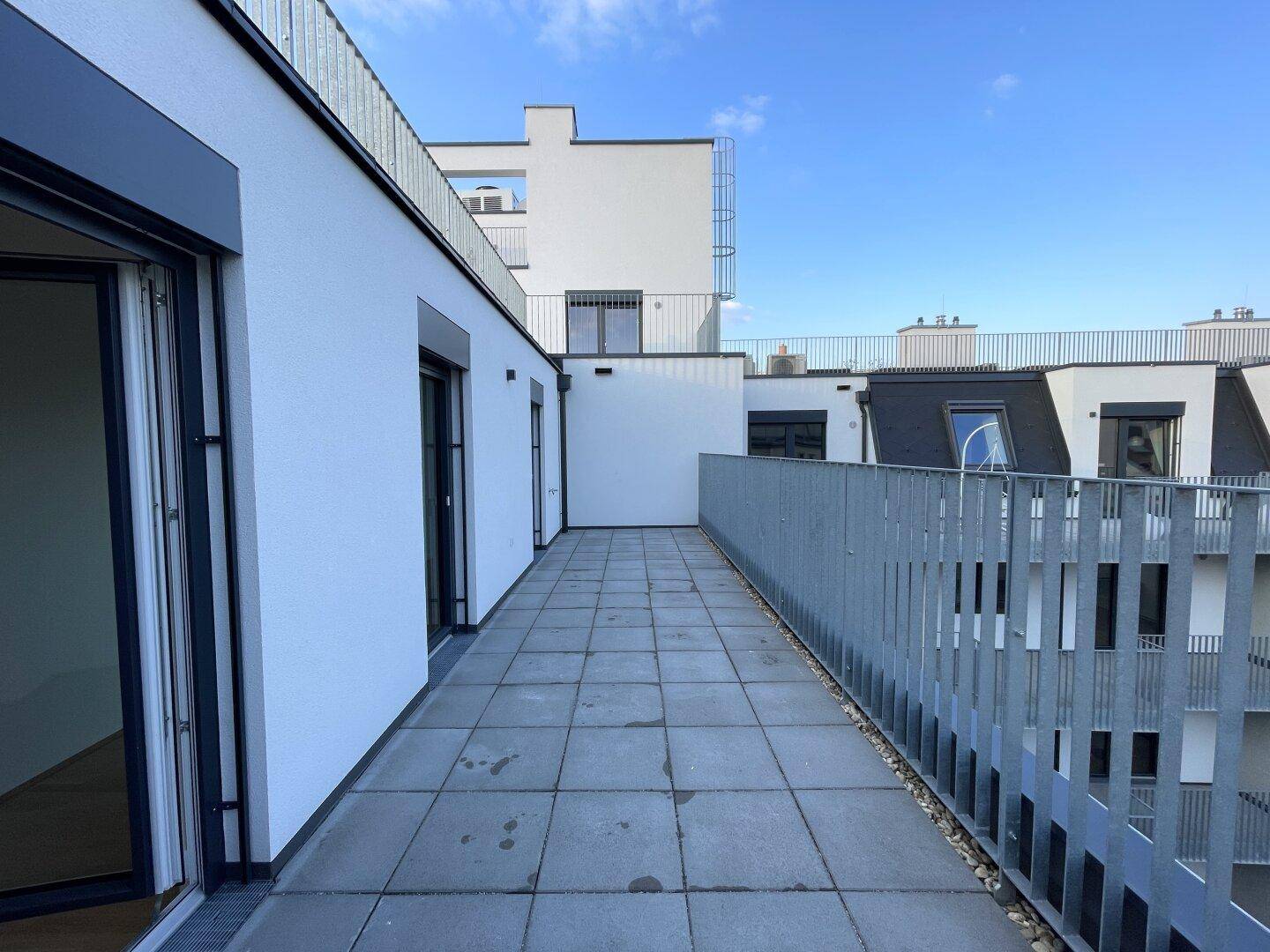 Weitläufige Dachterrasse mit Metallgeländer und Blick auf die umliegenden Gebäude und den Himmel.