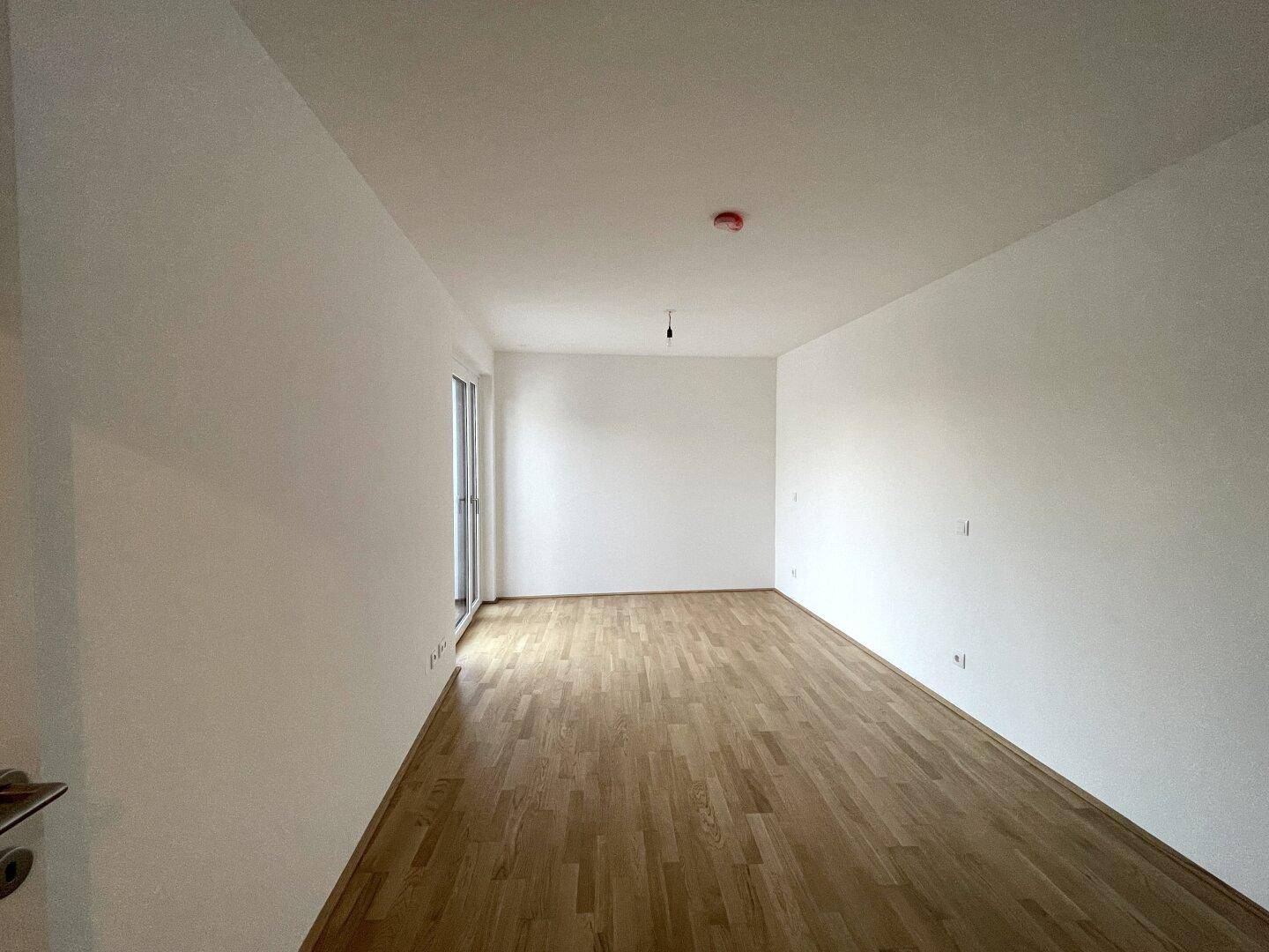 Helles Schlafzimmer mit Parkettboden und Zugang zu einem Außenbereich.
