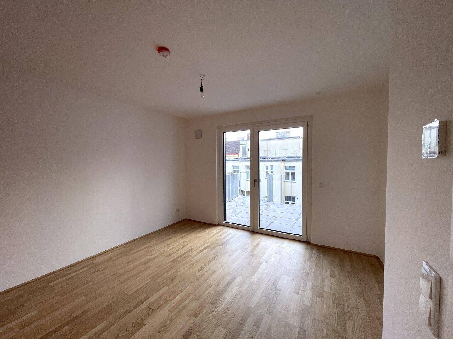 Heller Wohnraum mit großen Fenstern und Blick auf die umliegenden Gebäude.