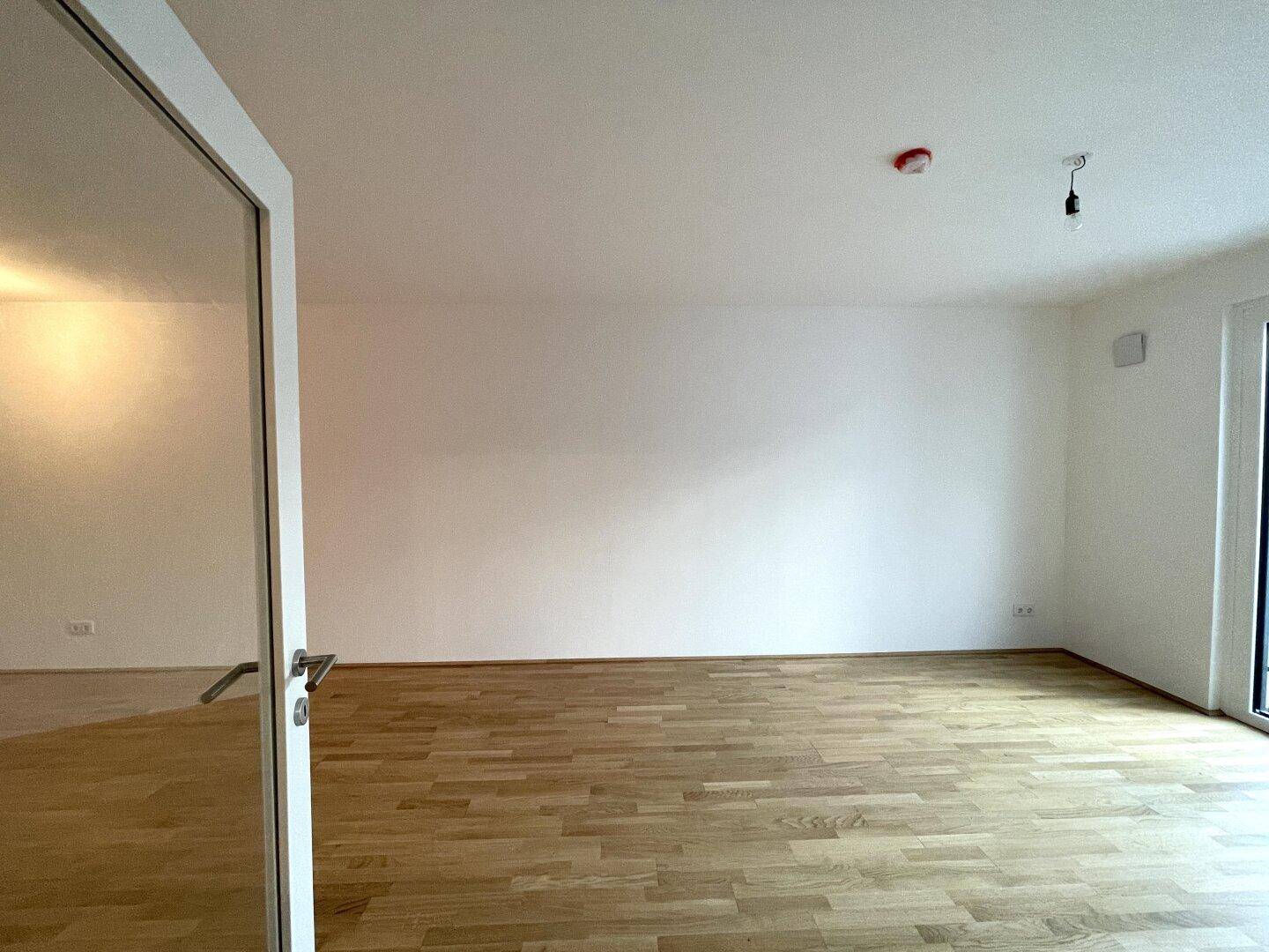 Geräumiger, leerer Wohnbereich mit Parkettboden und viel Tageslicht.