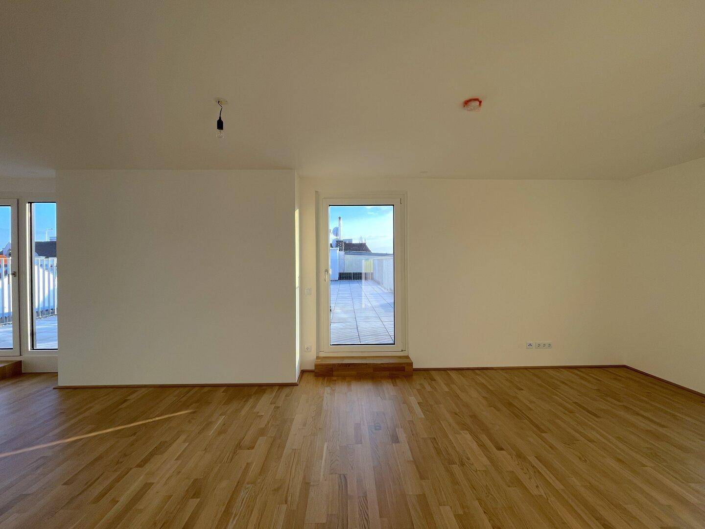Heller Raum mit Parkettboden und zwei Zugängen zu Außenbereichen, ideal als Wohnzimmer.