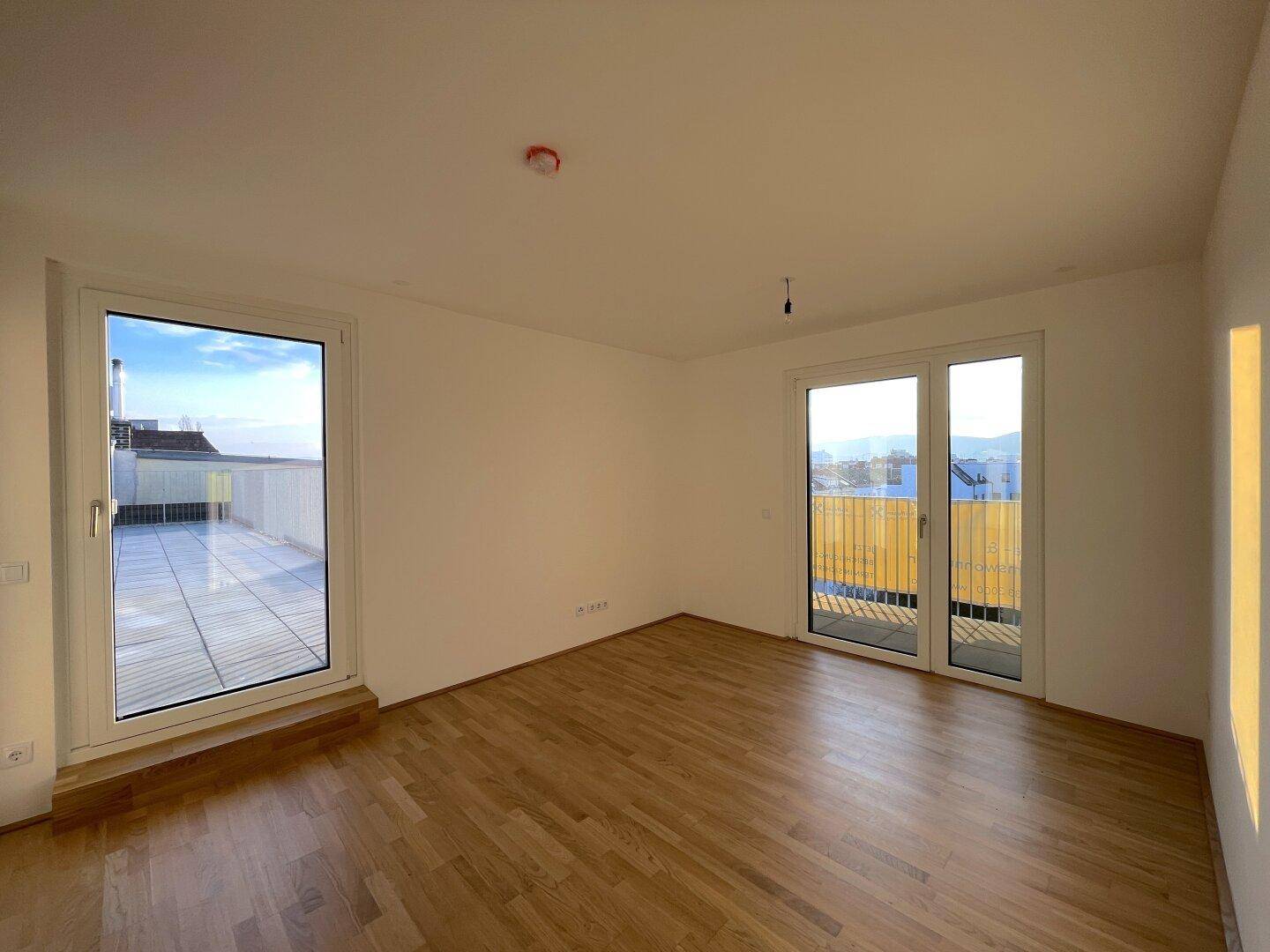 Lichtdurchfluteter Wohnbereich mit Holzboden und direktem Zugang zu Balkon und Terrasse.