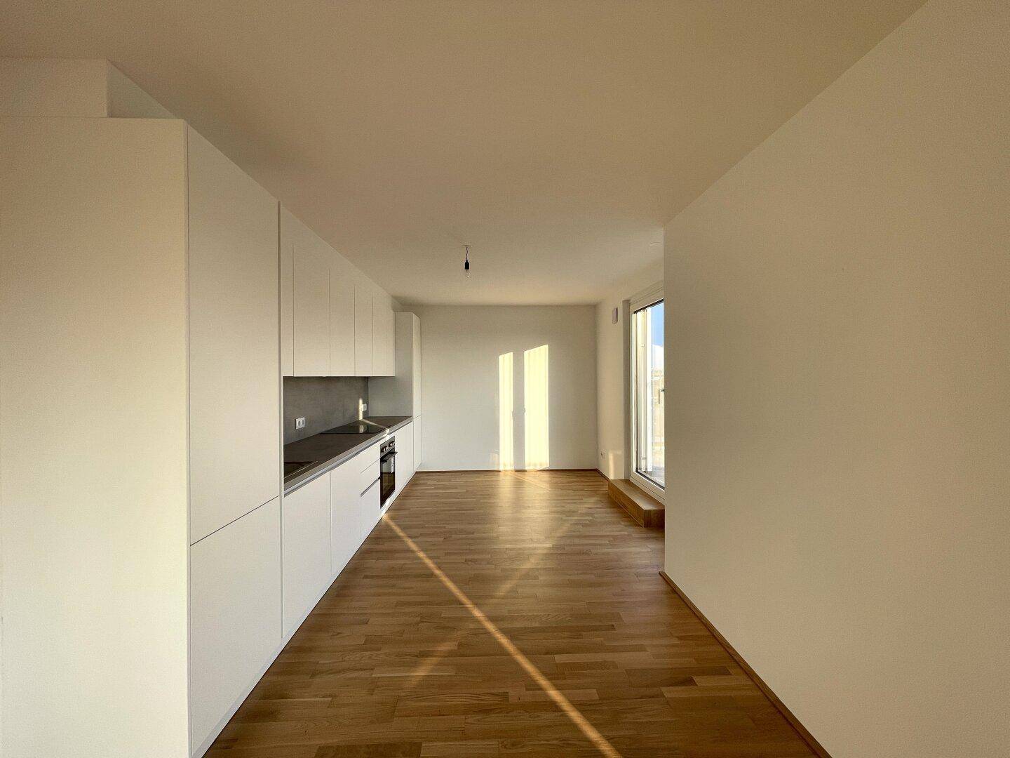 Moderne, offene Küche mit weißen Schränken, integrierten Geräten und Holzboden.
