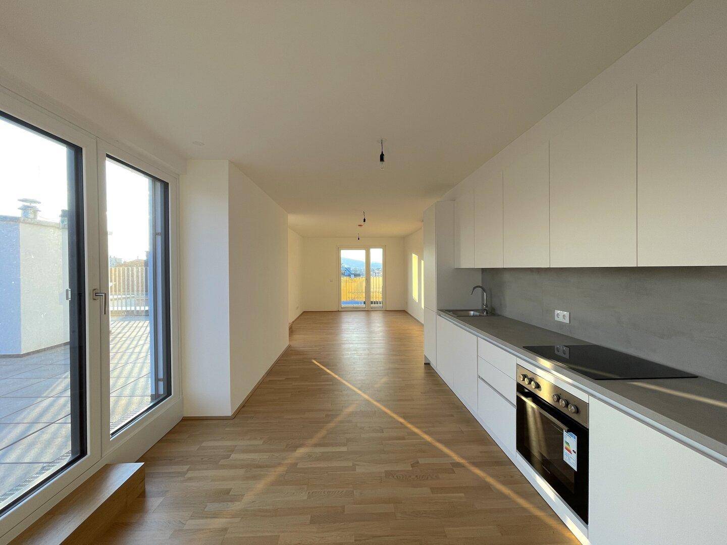 Helle Küche mit Induktionskochfeld, Backofen und Zugang zur Terrasse mit Weitblick.