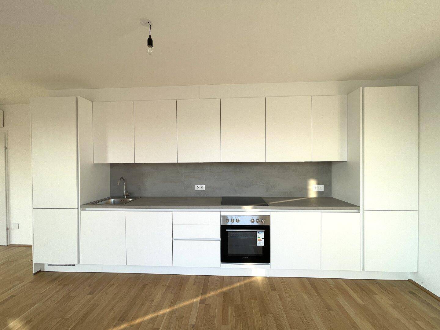 Detailansicht der modernen Einbauküche mit weißen Fronten, Spüle, Kochfeld und Backofen.