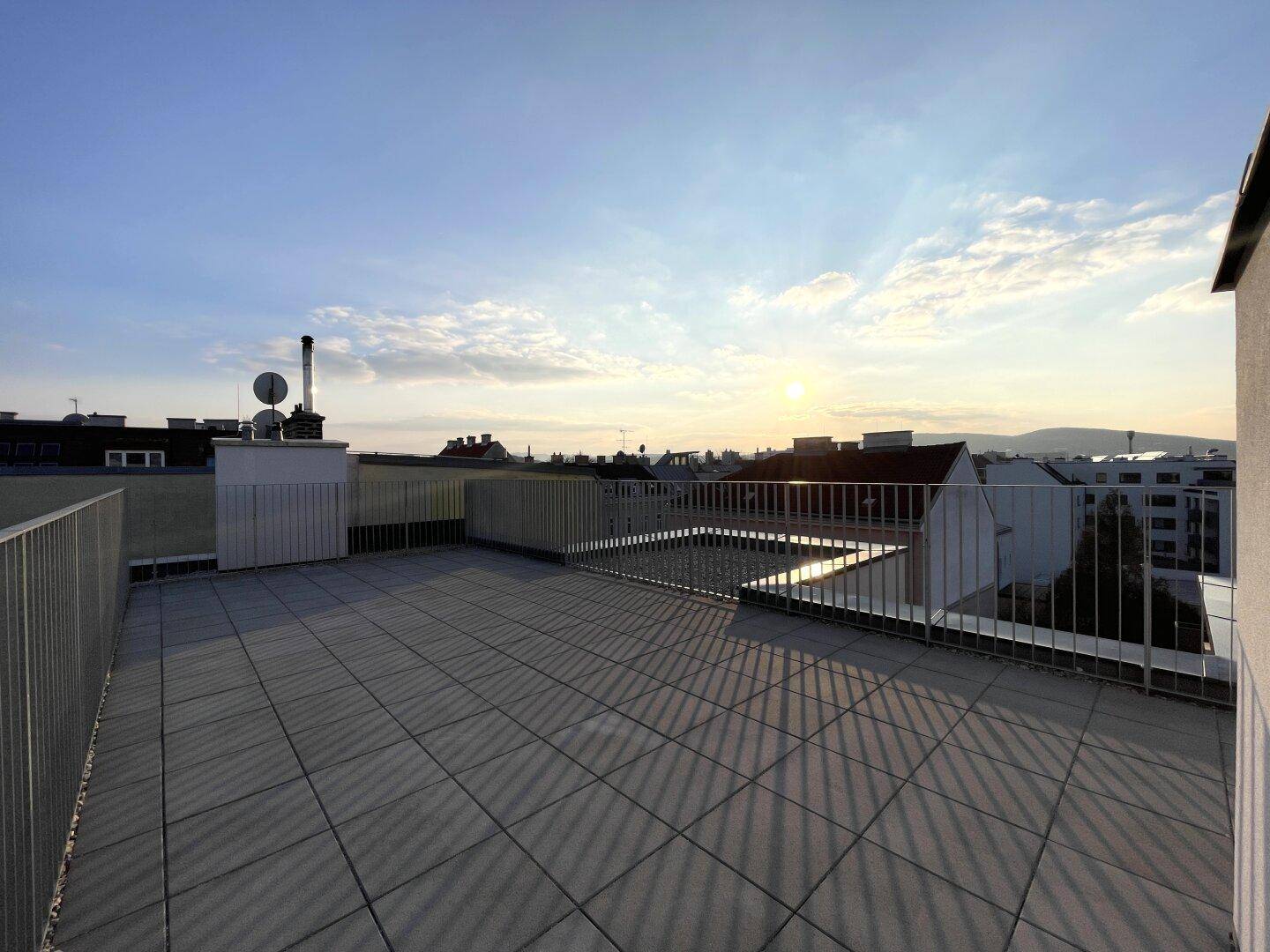 Große, geflieste Dachterrasse mit Metallgeländer und weitem Blick über die Dächer der Stadt.