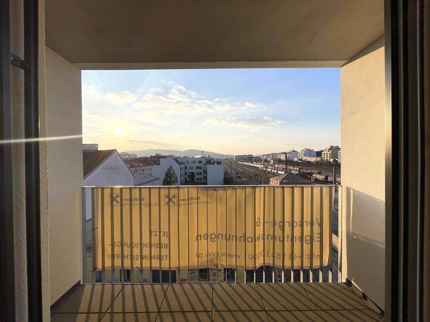 Balkon mit Blick auf die Stadt und die Bahngleise, mit einem Werbebanner.