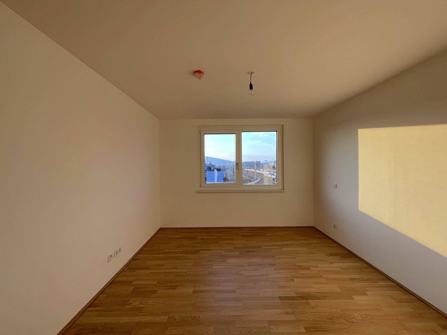 Helles Schlafzimmer mit Parkettboden und Fensterblick auf die Stadt und Umgebung.