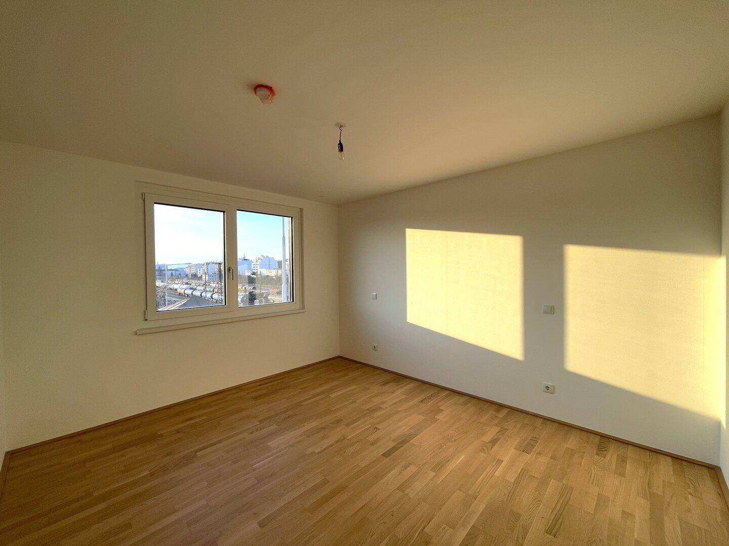 Lichtdurchflutetes Zimmer mit Holzboden und weitem Ausblick, ideal als Schlaf- oder Arbeitszimmer.