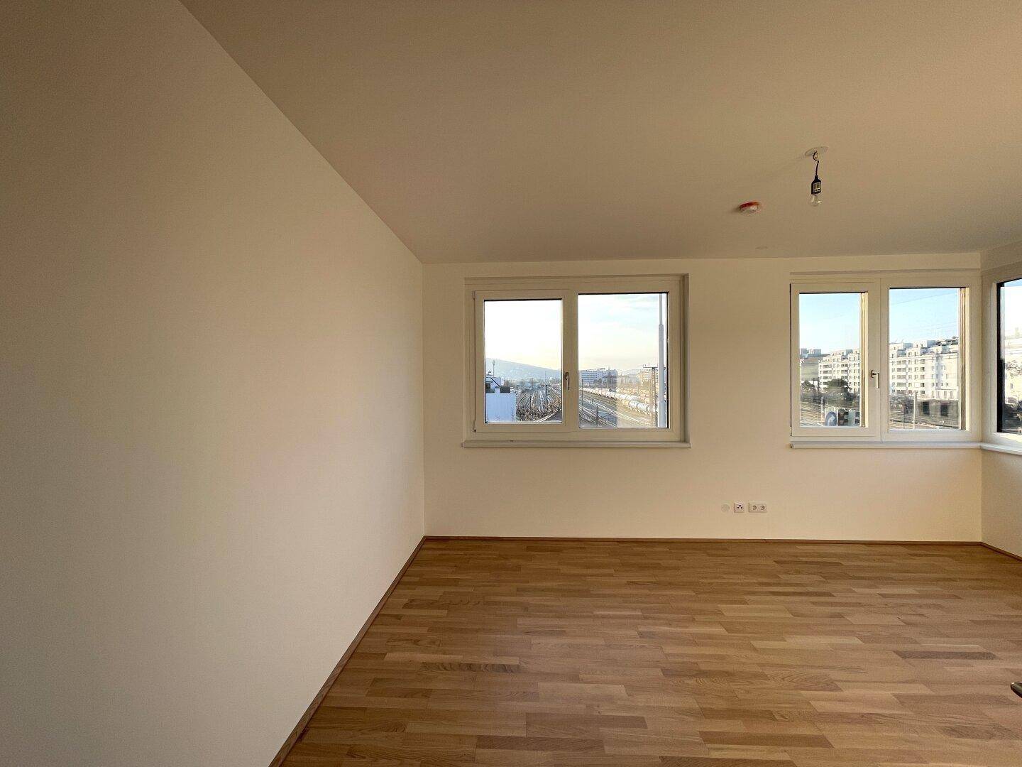 Helles Zimmer mit Parkettboden und zwei Fenstern, die einen urbanen Ausblick bieten.