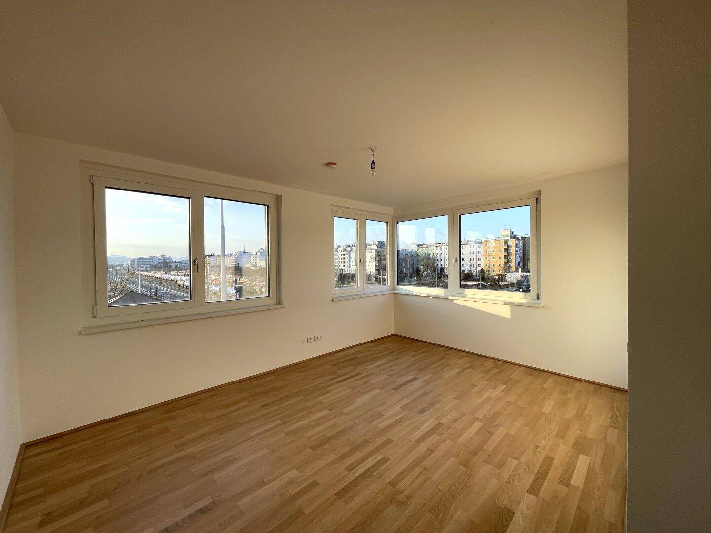 Eckzimmer mit Parkettboden und großen Fenstern, die einen weiten Stadtblick ermöglichen.