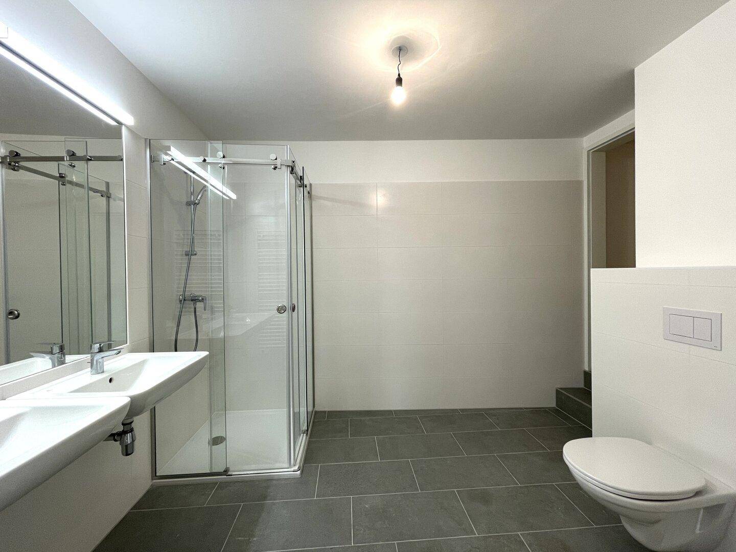 Modernes Badezimmer mit Doppelwaschbecken, begehbarer Dusche und Wand-WC.