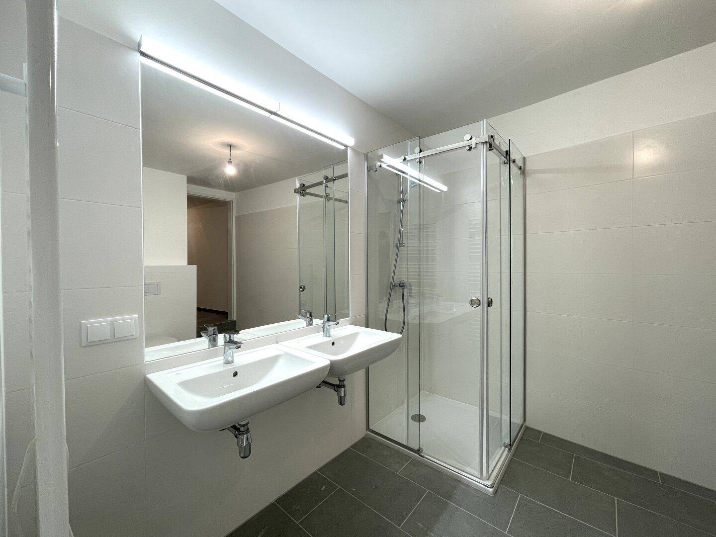 Elegantes Badezimmer mit zwei Waschbecken, großer Duschkabine und modernen Armaturen.