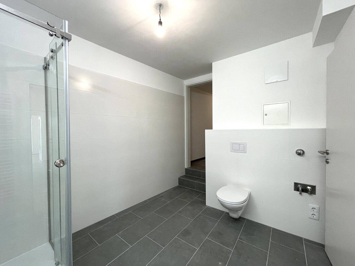 Modernes Badezimmer mit Duschkabine und wandhängendem WC, ausgestattet mit grauen Fliesen.