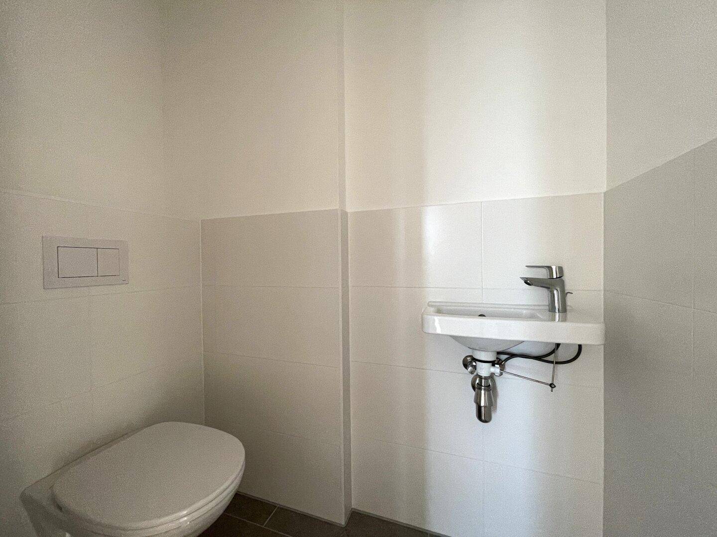 Kompaktes Gäste-WC mit wandhängender Toilette und kleinem Waschbecken, in hellen Farben gehalten.