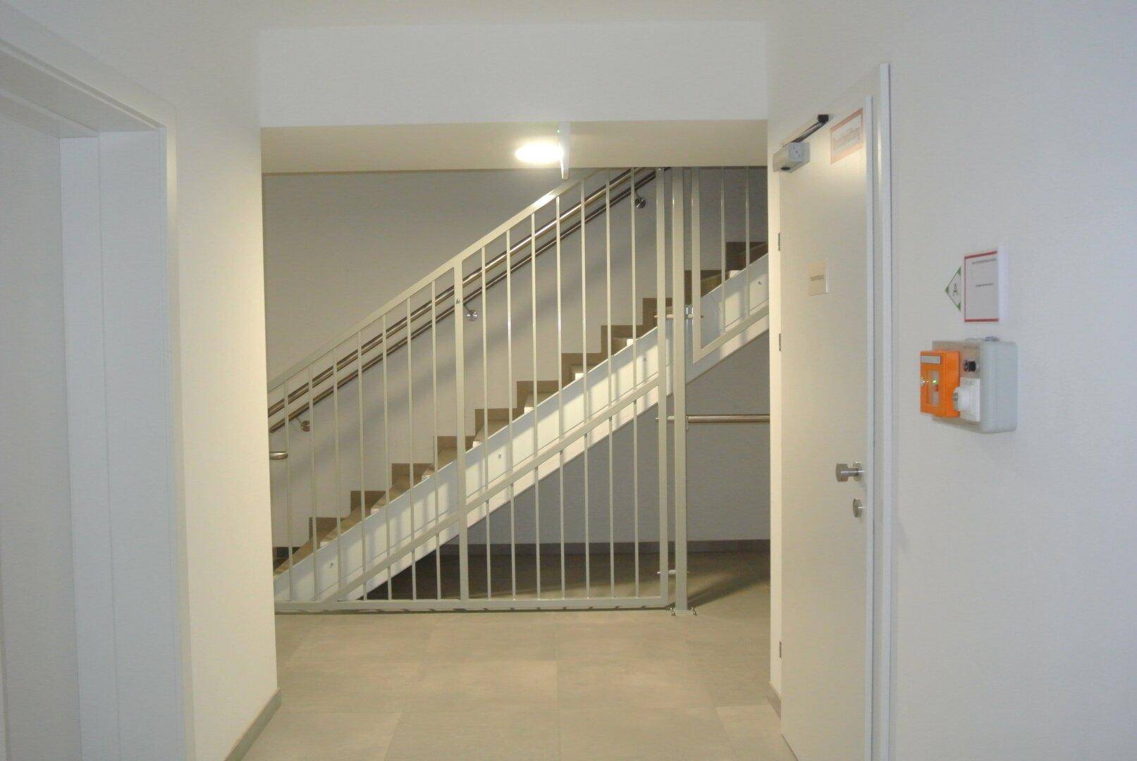 Heller Treppenaufgang in einem modernen Gebäude mit weißen Wänden und Fliesenboden.