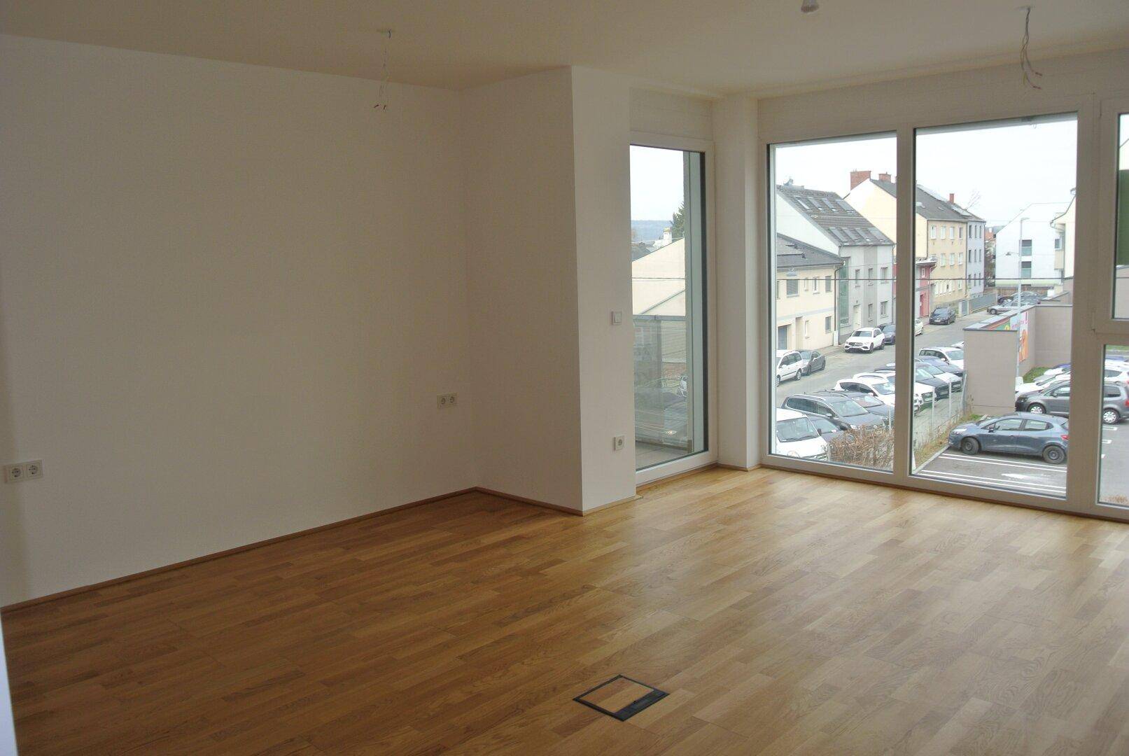 Geräumiges Wohnzimmer mit hellem Parkettboden und weitem Blick auf die Umgebung.