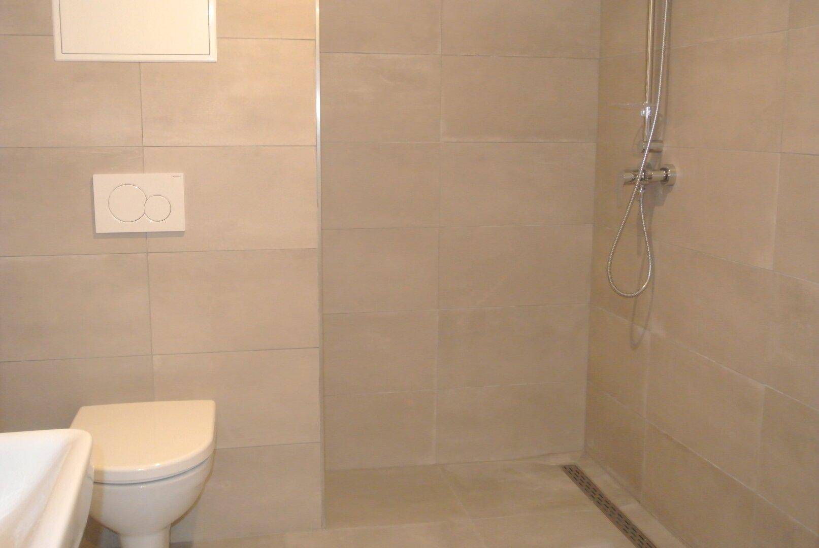 Modernes Badezimmer mit beigefarbenen Fliesen, wandhängendem WC und Duschbereich.