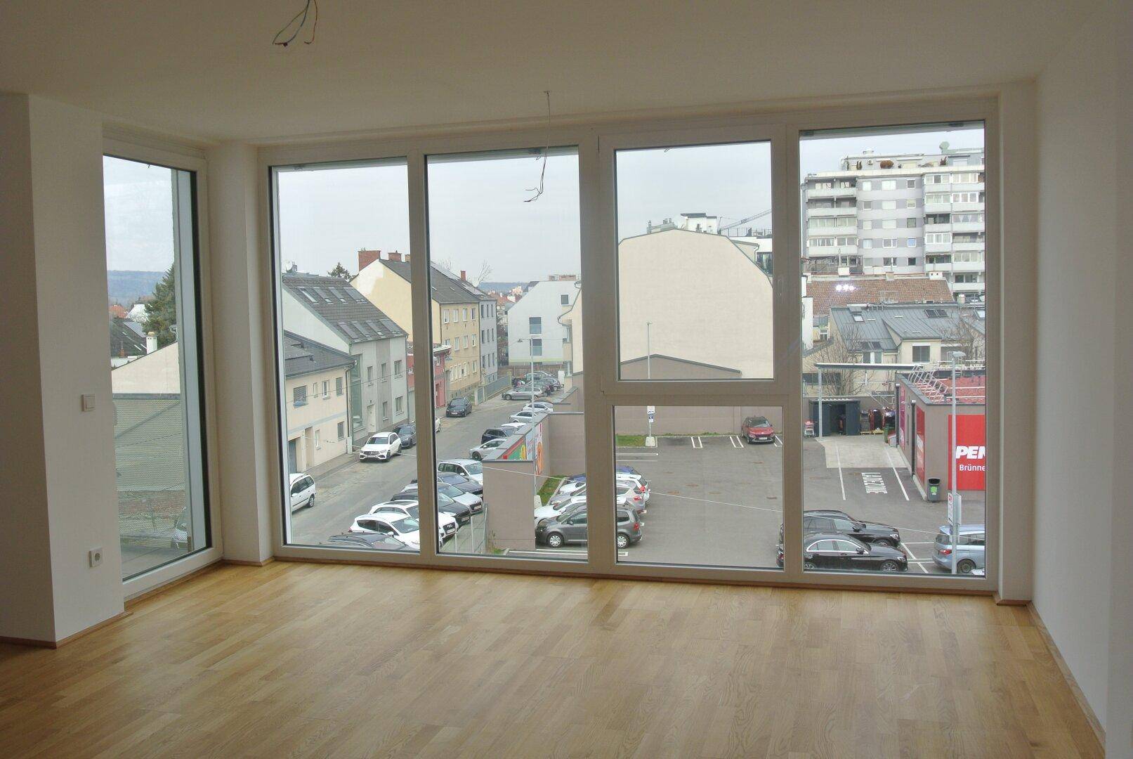 Heller, leerer Raum mit großen Fenstern und Blick auf die Stadt und umliegende Gebäude.