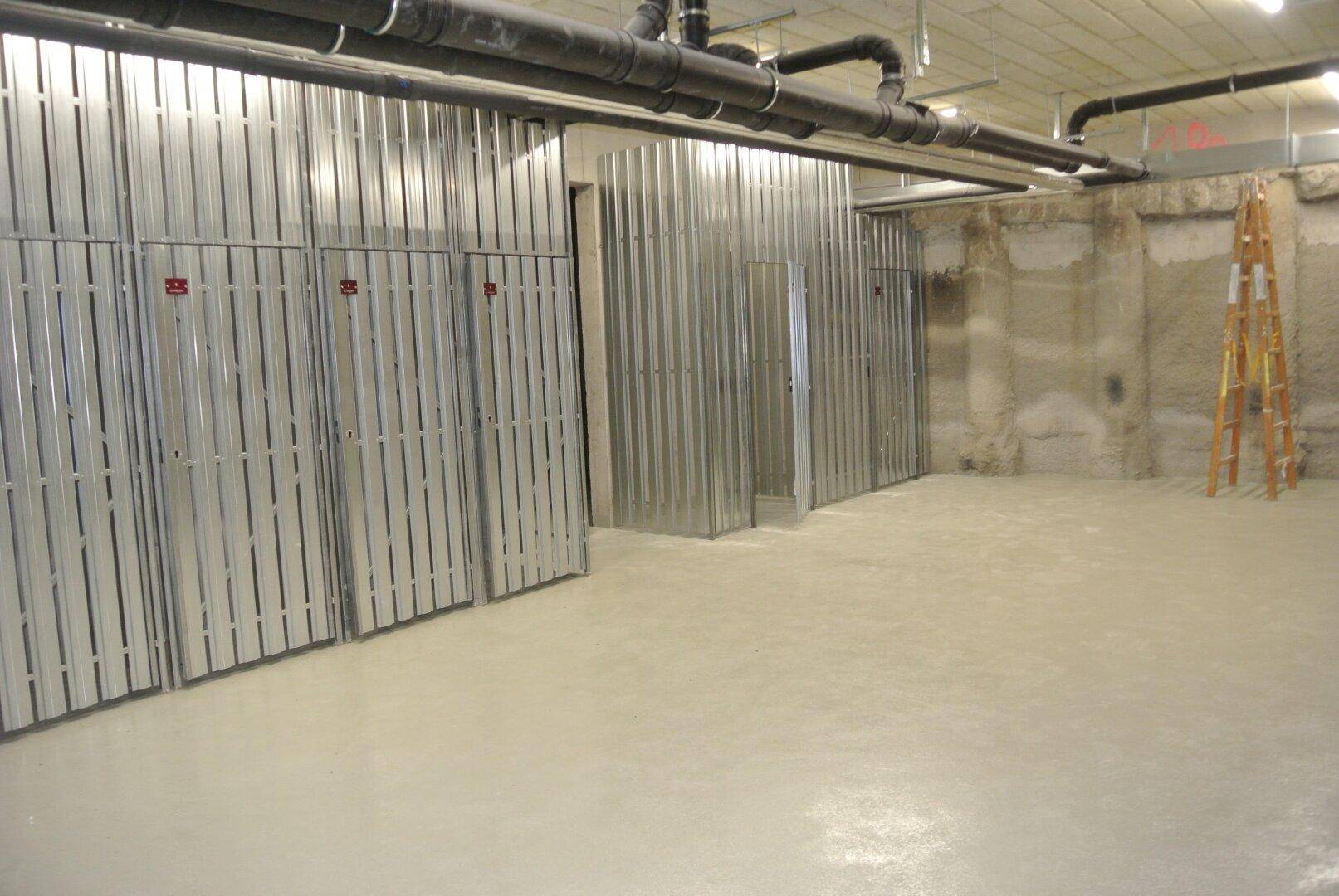 Geräumiger Kellerraum mit Metallabtrennungen für Abteile und sichtbaren Rohrleitungen an der Decke.