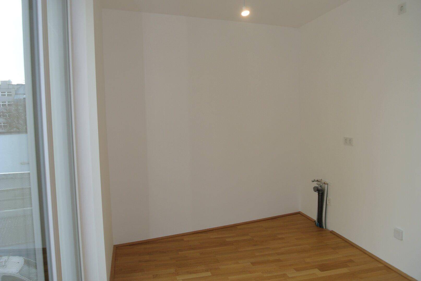 Leerer Raum mit Holzboden und sichtbaren Wasseranschlüssen, ideal für eine Küche oder Hauswirtschaftsraum.