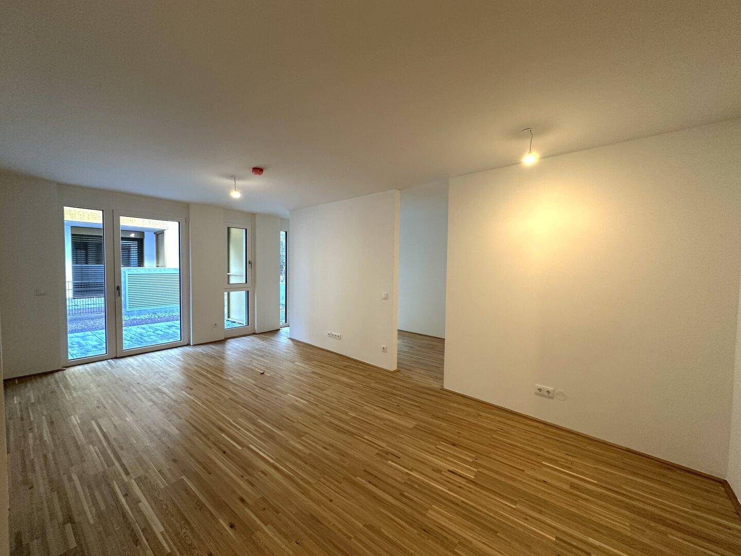 Geräumiger, unmöblierter Wohnbereich mit großen Fenstern und Holzboden.