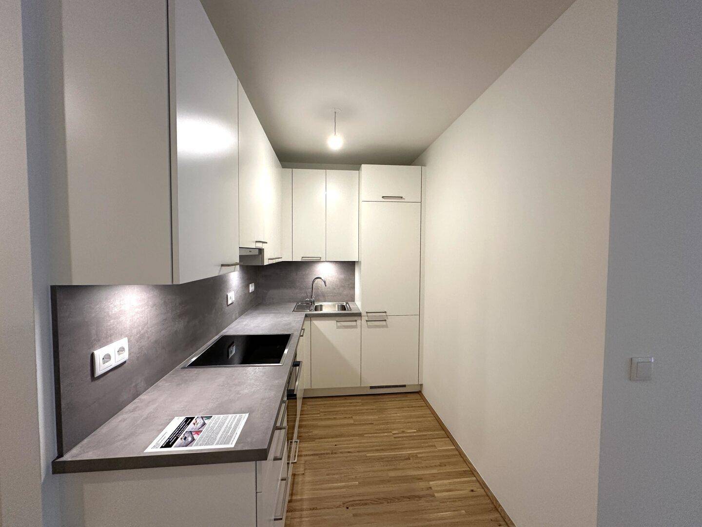 Moderne Einbauküche mit weißen Schränken, dunkler Arbeitsplatte und integriertem Kochfeld.