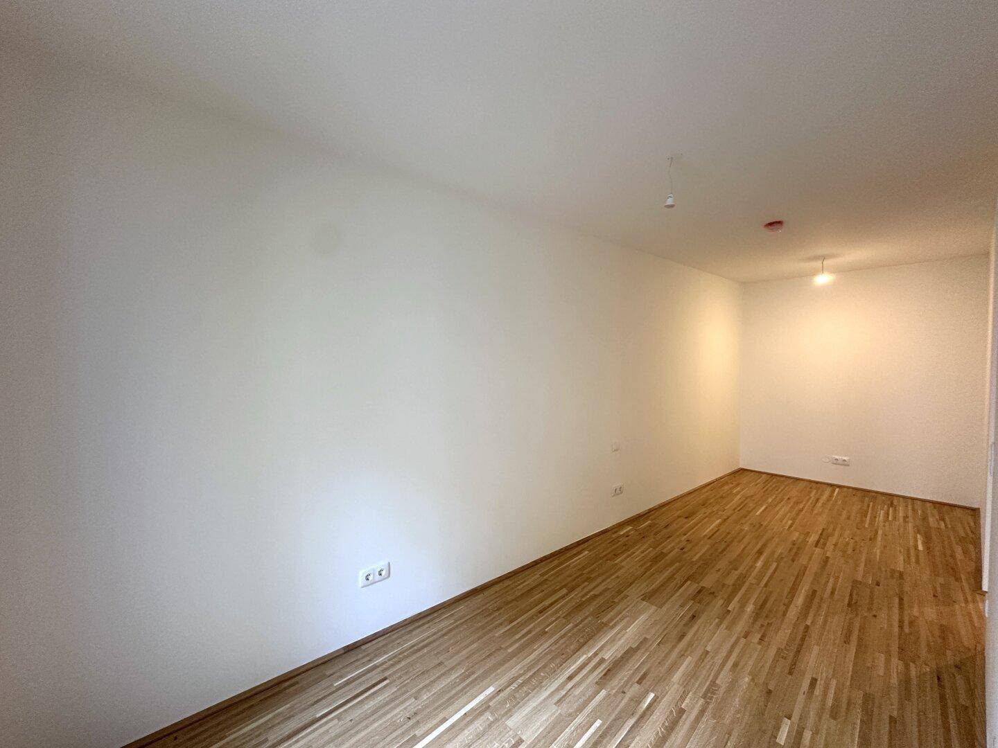 Leeres Schlafzimmer mit hellem Parkettboden und weißen Wänden, bereit zum Einzug.